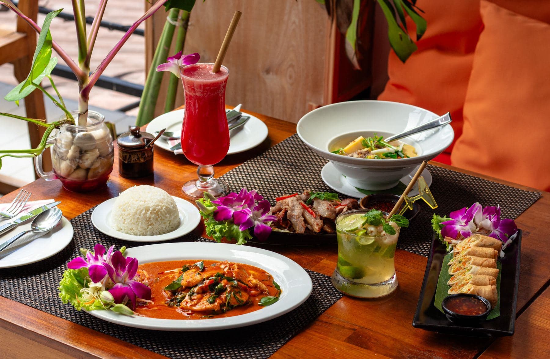 Gedeckter Tisch mit rotem Curry, Reis, Frühlingsrollen und Getränken